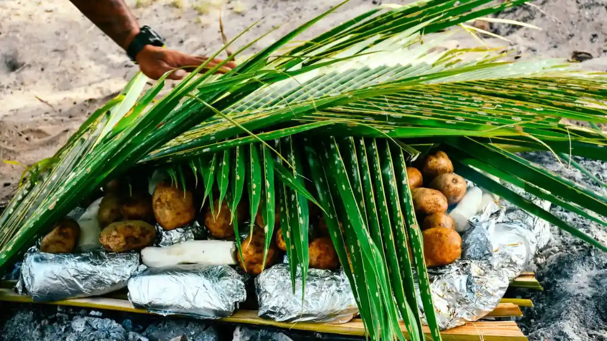 Foil-wrapped food and root crops covered with green leaves while preparing a Fijian lovo earth oven
