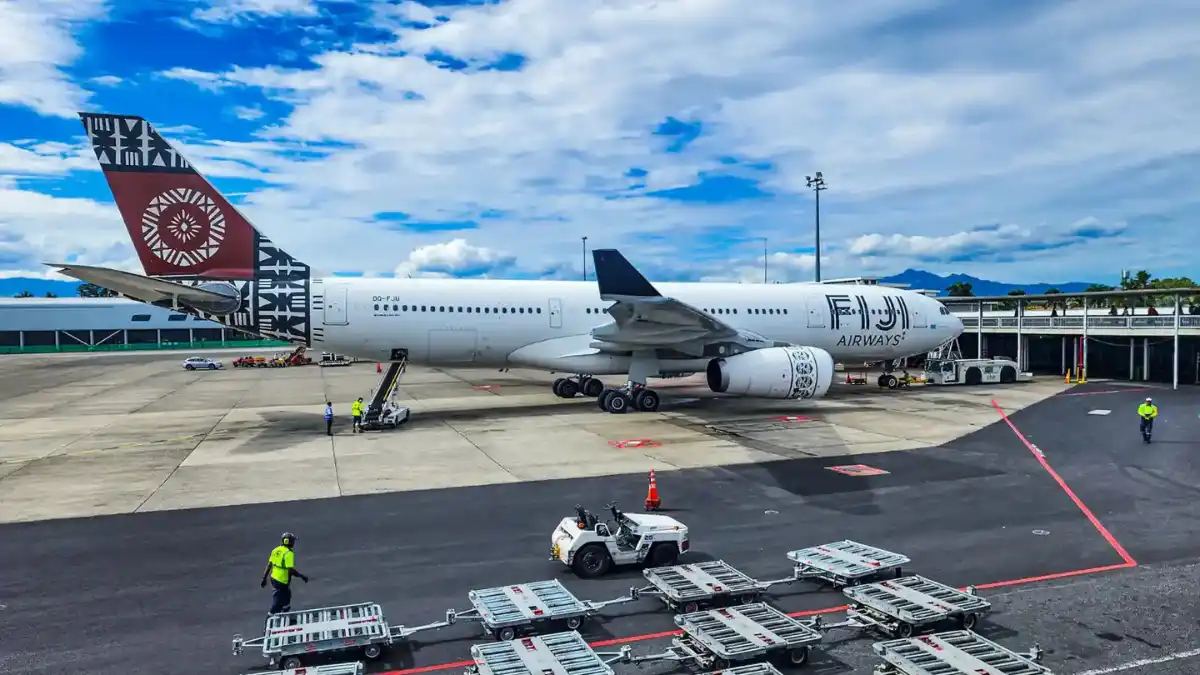 Fiji Airways aircraft parked beside an airport terminal with ground staff and baggage carts
