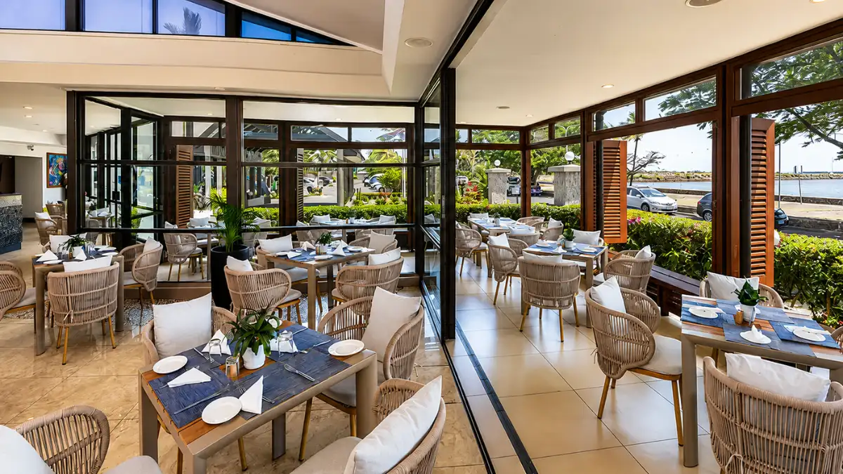Dining room at Fins Restaurant in Lautoka with set tables, large windows and the waterfront visible outside.