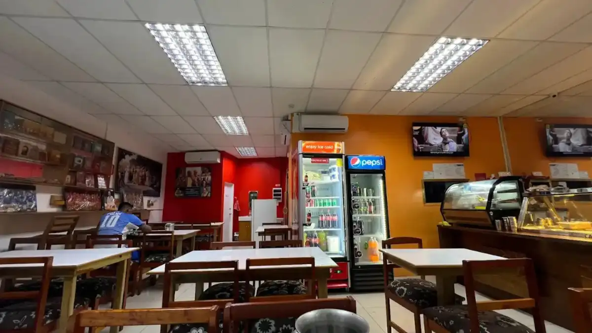 Dining room inside Hare Krishna Restaurant in Nadi, with tables, drink refrigerators and a food counter.