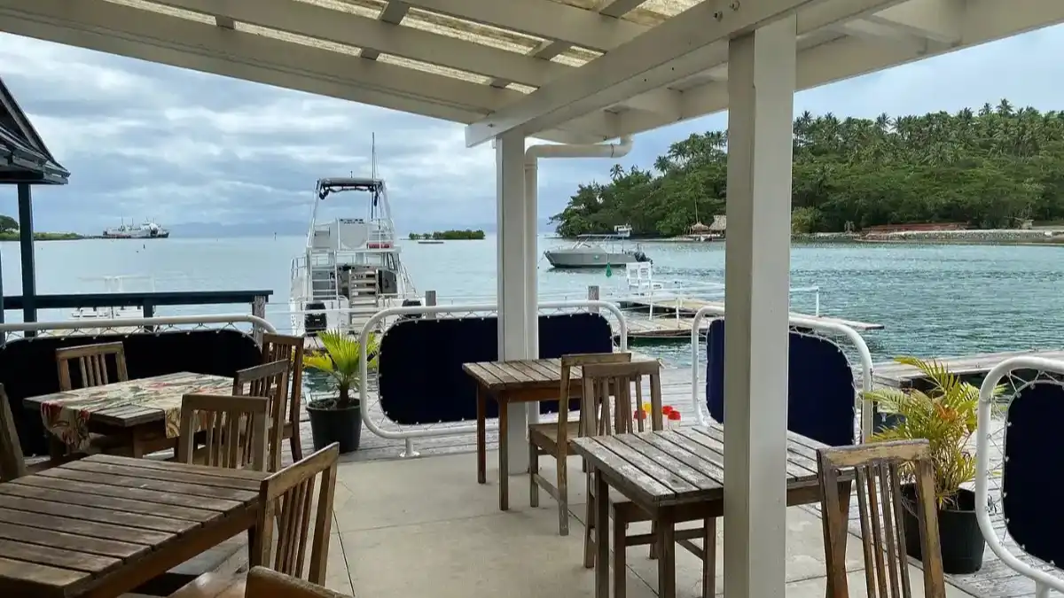 Wooden tables on the covered waterfront deck at Captain's Cafe overlooking boats in Savusavu harbour