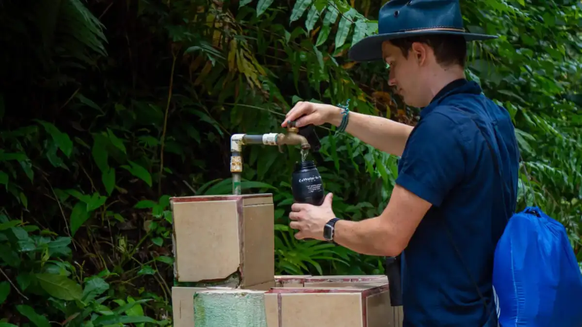 Traveler filling a reusable water bottle from an outdoor tap in a tropical setting