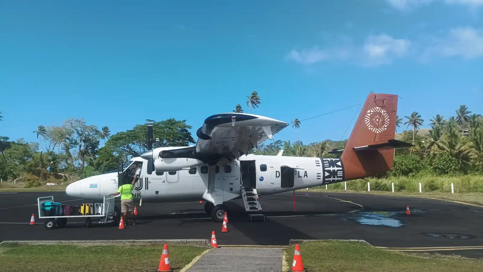 Fiji Link aircraft parked on the runway at Savusavu Airport, surrounded by lush tropical hills and the Koro Sea coastline
