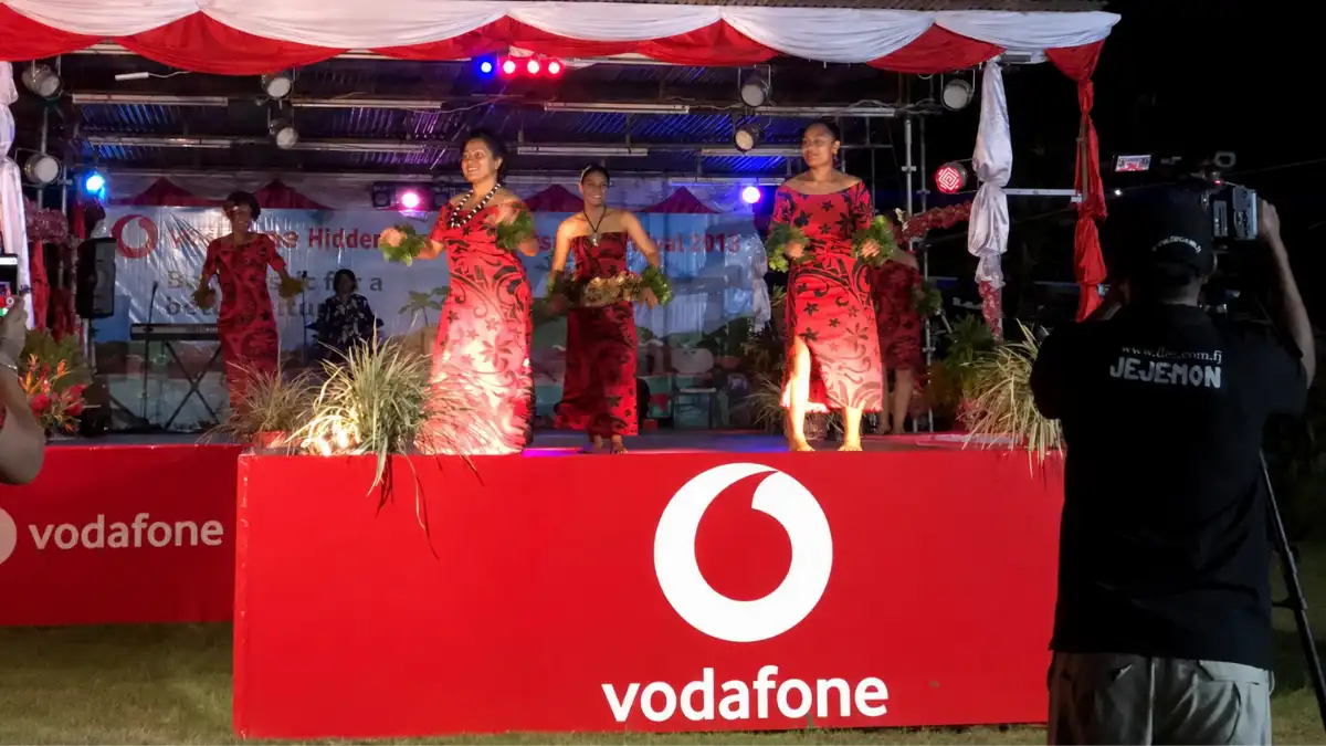 Performers in red outfits on a Vodafone-branded stage at an evening community event in Savusavu