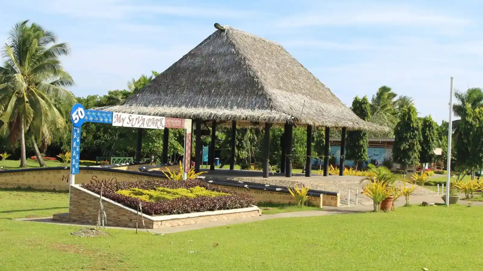 Locals relaxing under shade trees at My Suva Park with Suva Harbour and ocean views in background