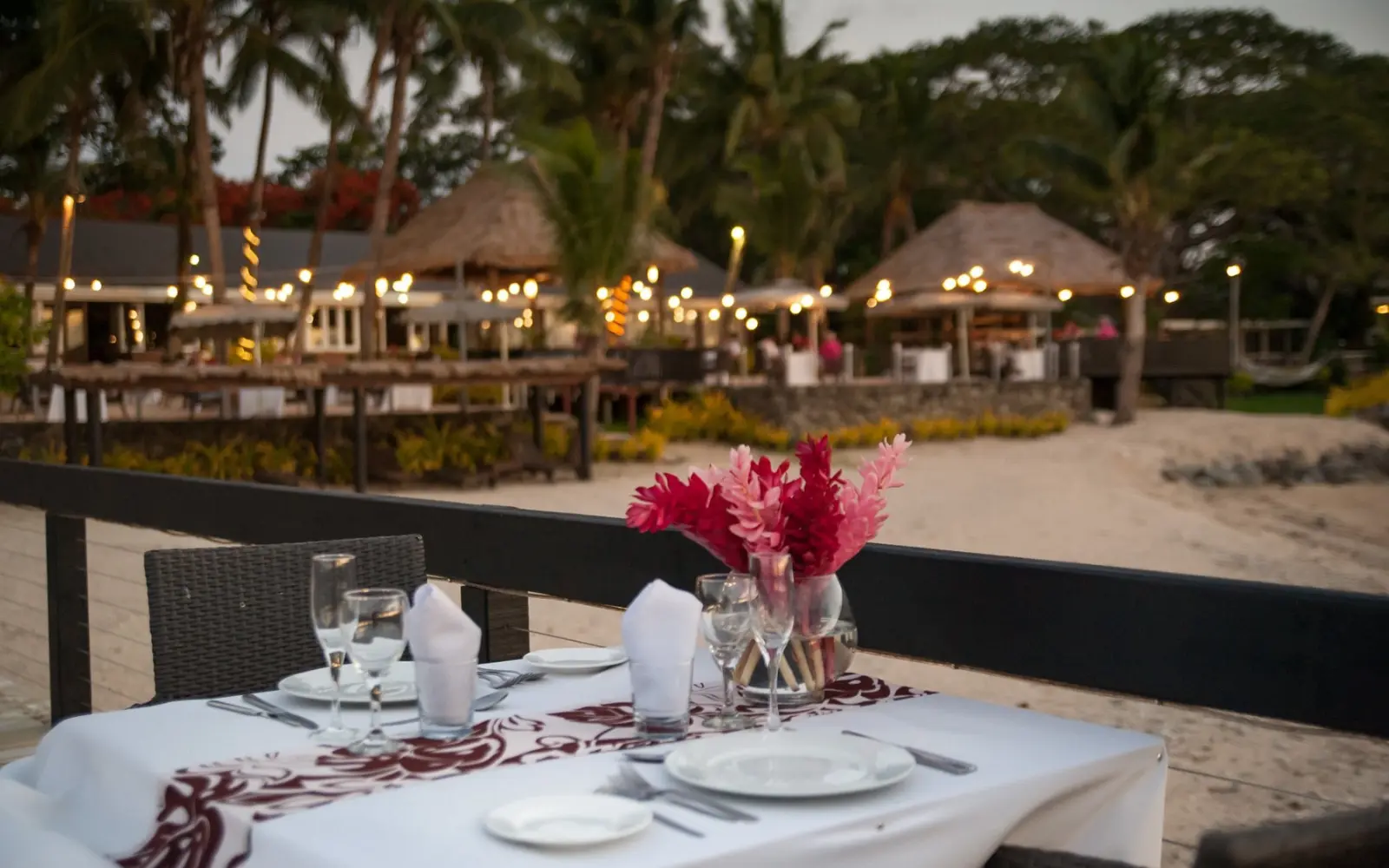A charming outdoor table and chairs set on the beachfront of First Landing Beach Resort in Fiji, with the resort building visible in the peaceful background.