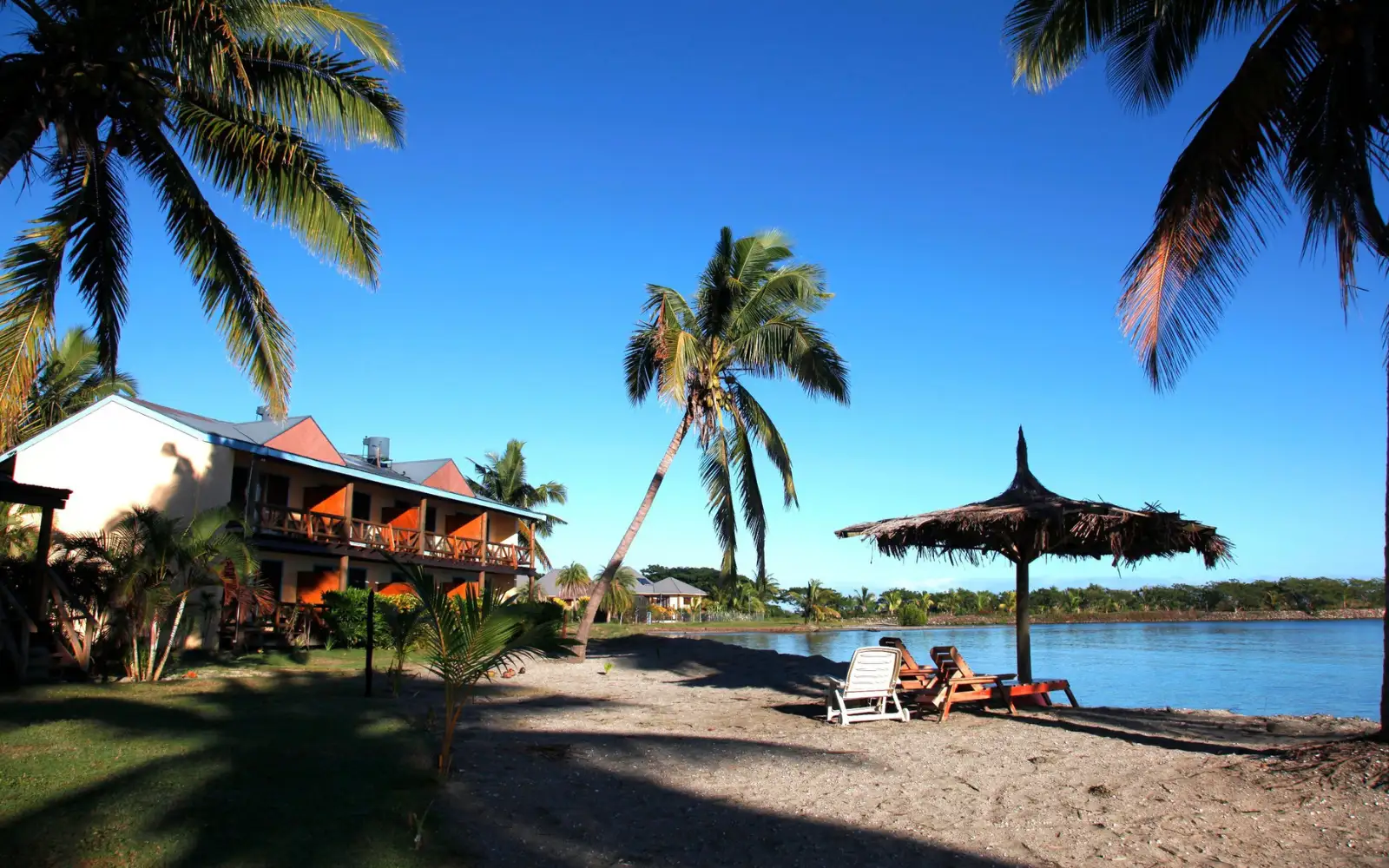 Traditional Fijian thatched bures of Club Fiji Resort nestled directly on a calm sandy beach, facing the ocean near Nadi.