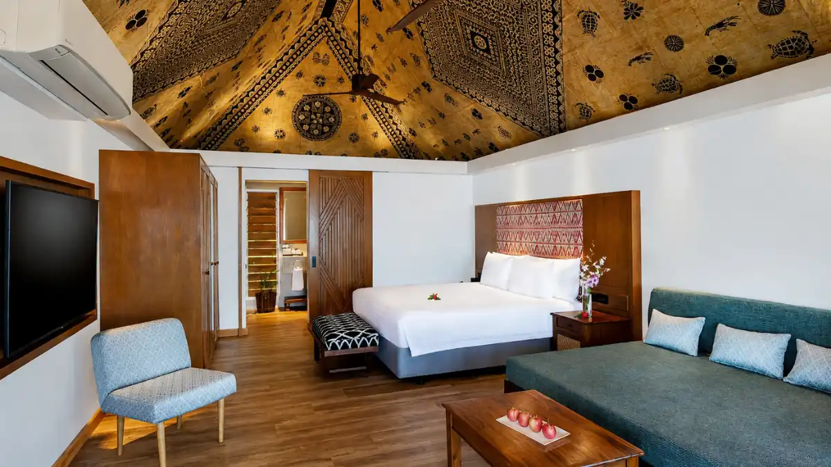 Interior of an Ocean Breeze Bure at Outrigger Fiji Beach Resort with a high ceiling, king bed, seating area and Fijian-inspired details.