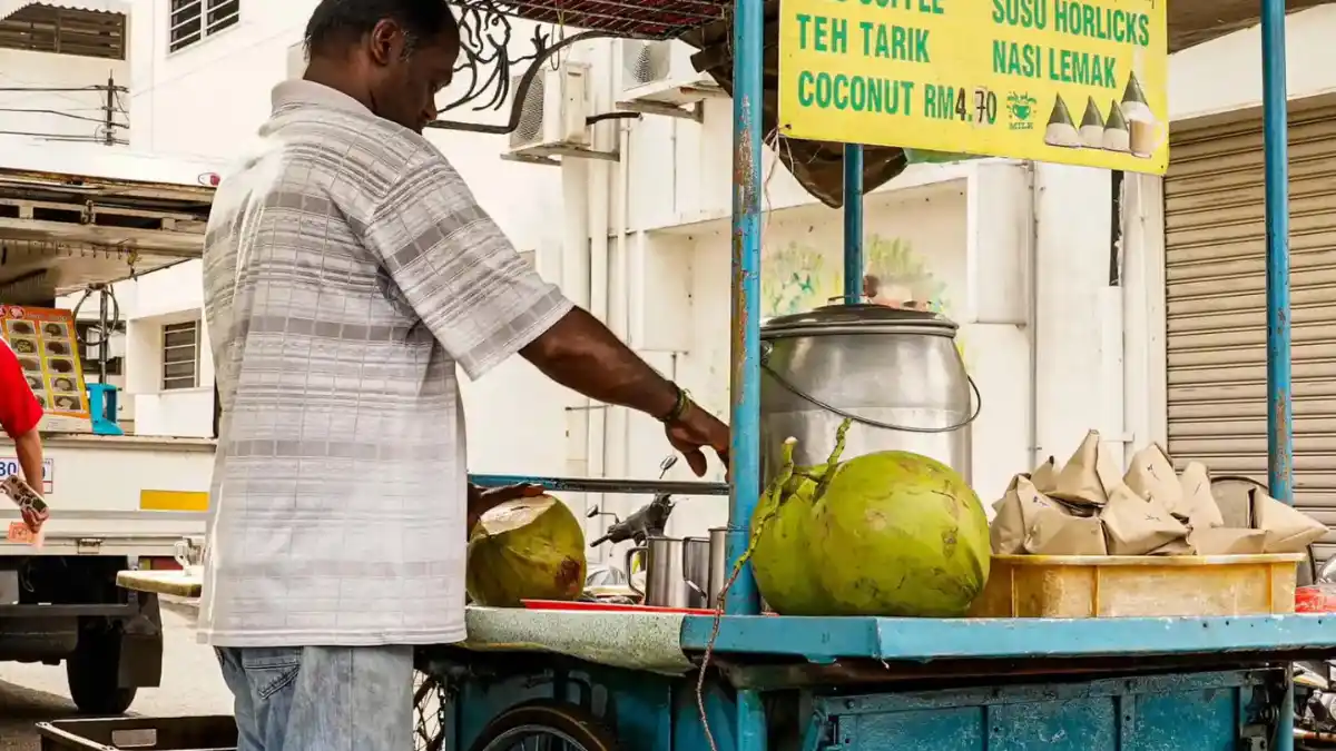 A vendor opening a fresh green coconut for a traveler at a produce market in Nadi, Fiji