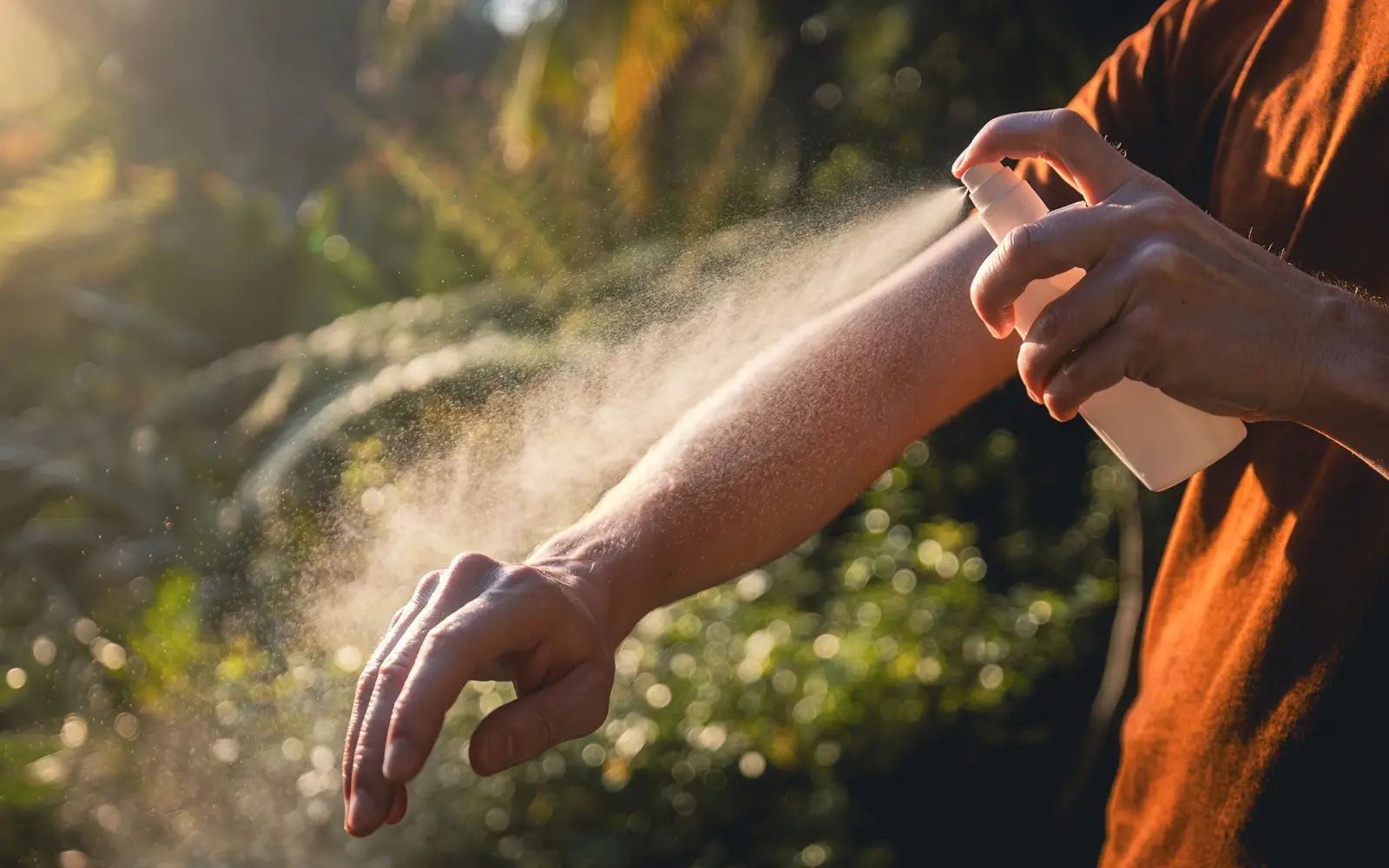 Traveler spraying mosquito repellent on arms before a rainforest hike in Sigatoka at dusk