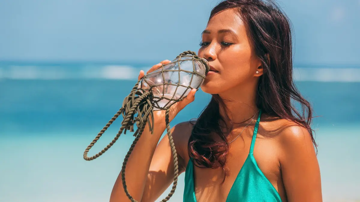 Woman drinking from a clear reusable bottle on a beach in Fiji