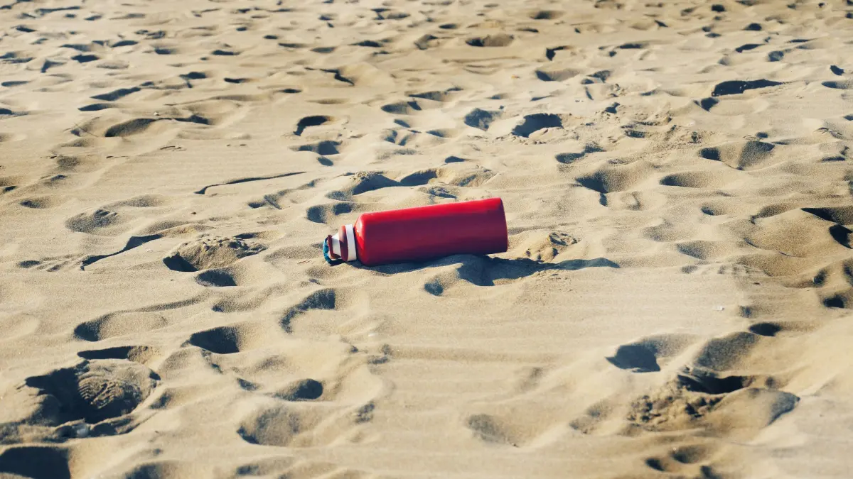 Red reusable water bottle resting on sand at a beach in Fiji