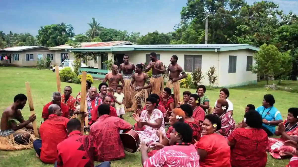Adult visitors in modest clothing sitting with local hosts during an organised village visit in Fiji