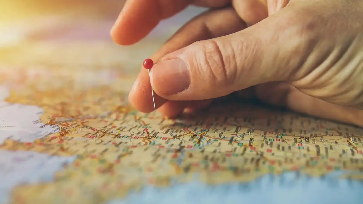 Hand placing a red pin on a paper map while planning a trip