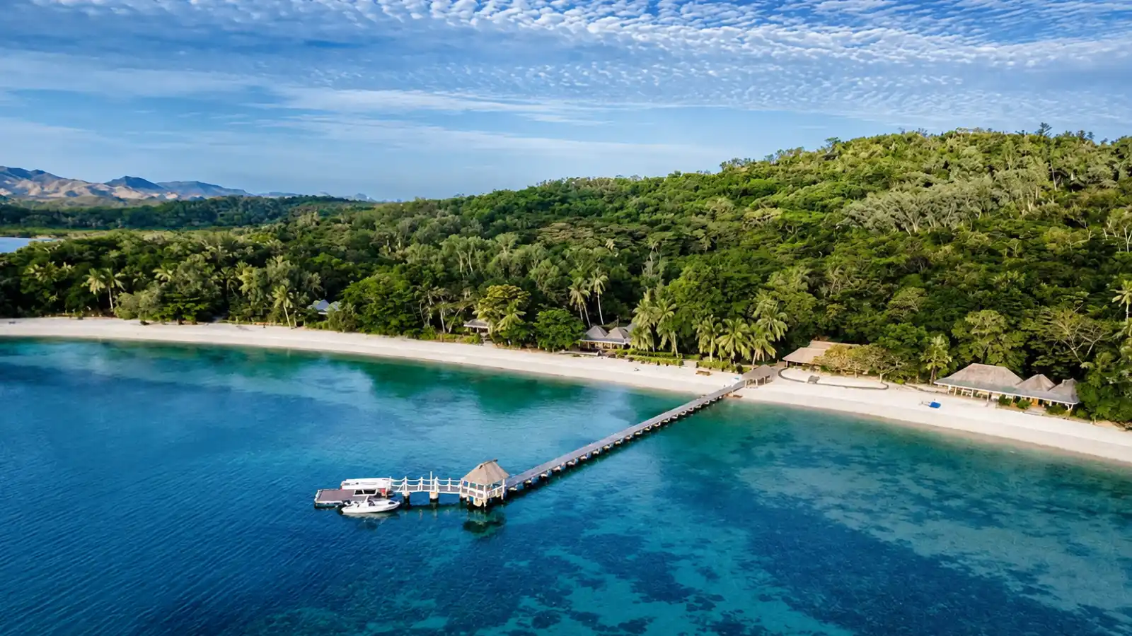 Aerial view of Turtle Island Fiji Resort with a white-sand beach, jetty, beachfront bures and clear lagoon water