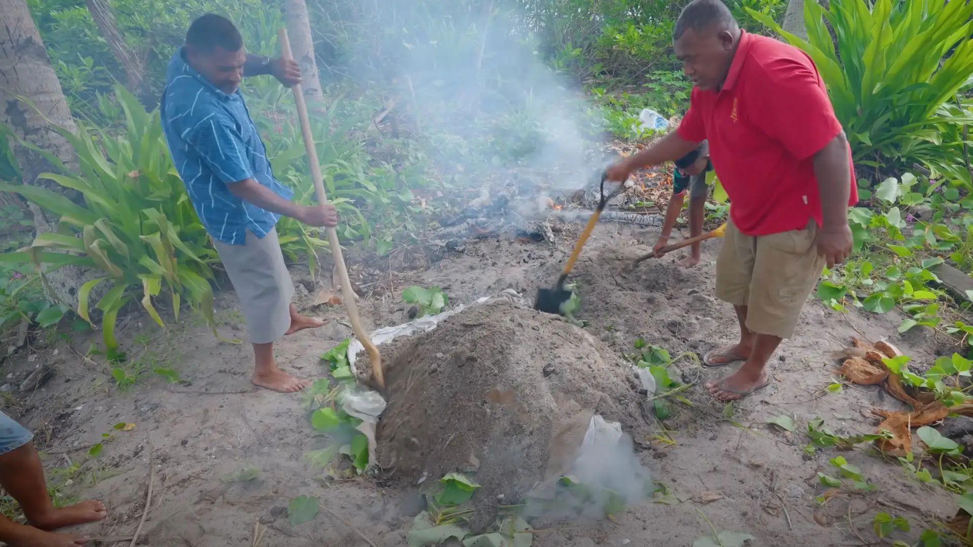 Fijian elder teaching visitors traditional lovo earth oven cooking in tropical village setting